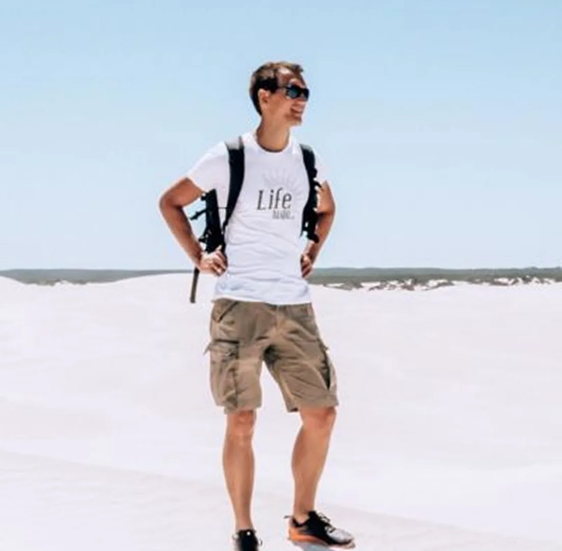 Daniel von Life to Go steht mit Rucksack in einer weißen Sandlandschaft und blickt in die Ferne