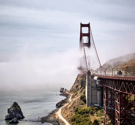 Golden Gate Bridge ragt aus dichtem Nebel über Küstenlandschaft.
