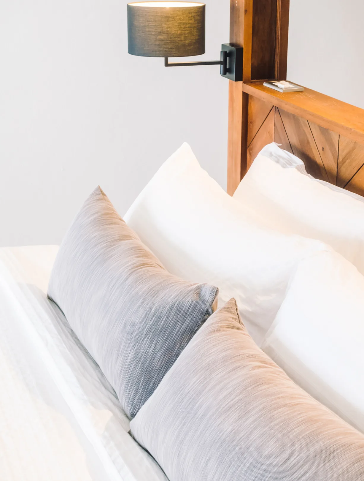 Gemachtes Bett mit Kissen und Wandlampe an einem Holzkopfteil.