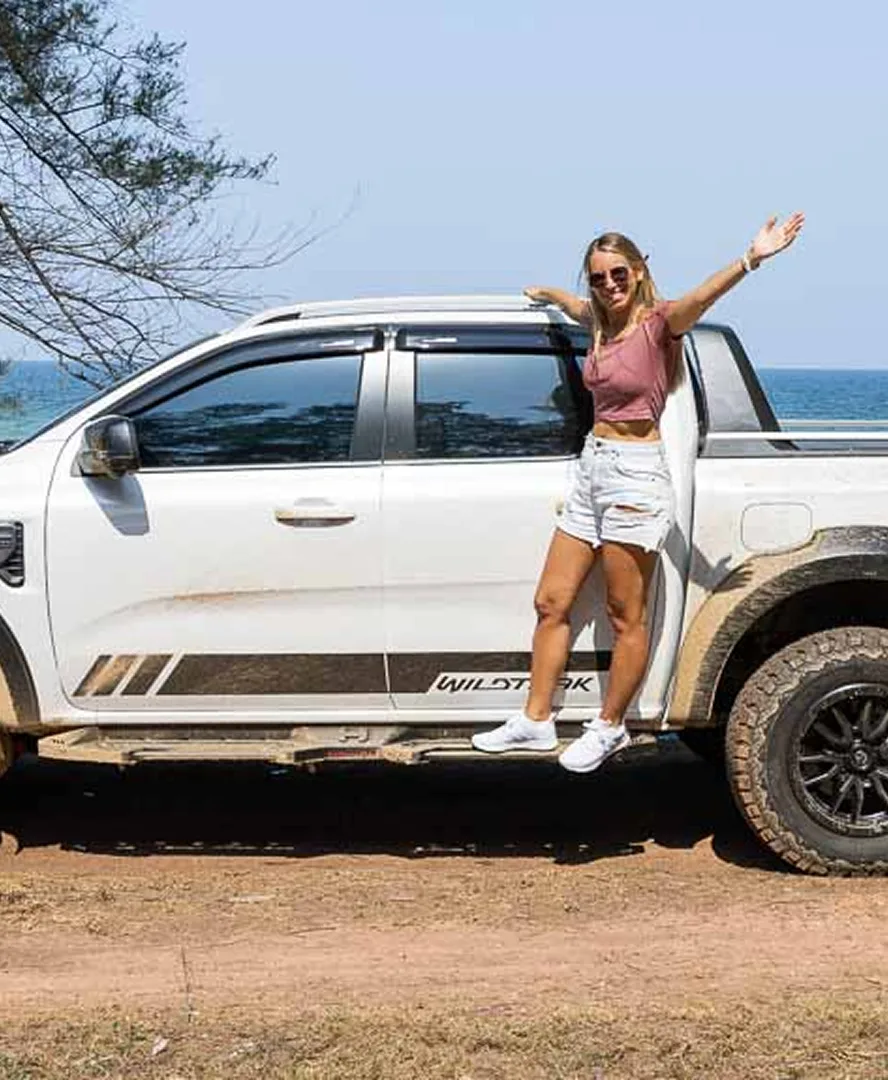 Frau steht auf einem Pickup am Strand und breitet die Arme aus.