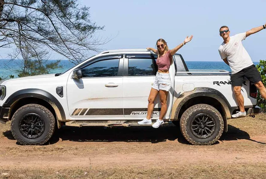 Paar steht auf einem Pickup am Strand und posiert fröhlich für ein Foto.
