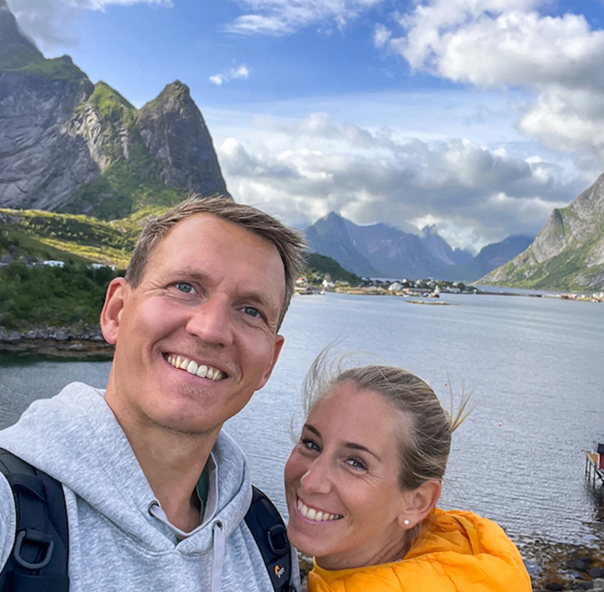 Paar macht ein Selfie vor Fjordlandschaft mit Bergen und Wasser im Hintergrund.