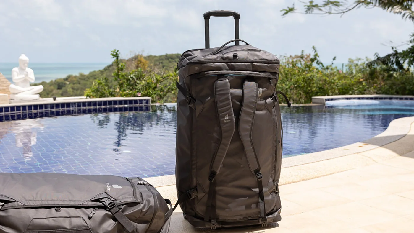 Reiserucksack und Tasche stehen am Pool mit Blick auf Meer und tropische Landschaft.