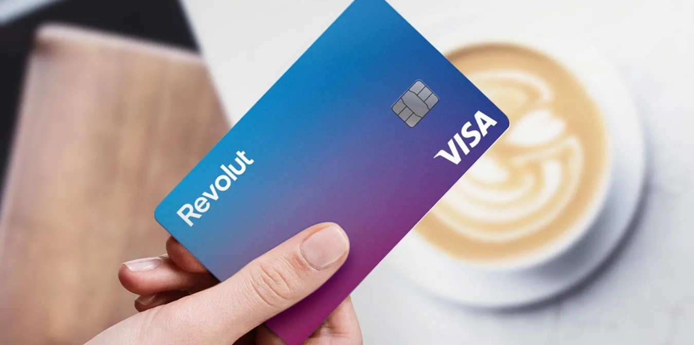 Hand hält Revolut Visa Karte vor unscharfem Hintergrund mit Kaffeetasse im Café.