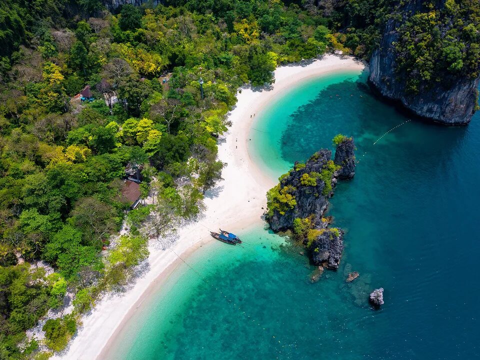 Tropische Bucht mit hellem Sandstrand, türkisfarbenem Wasser und dichter Vegetation.